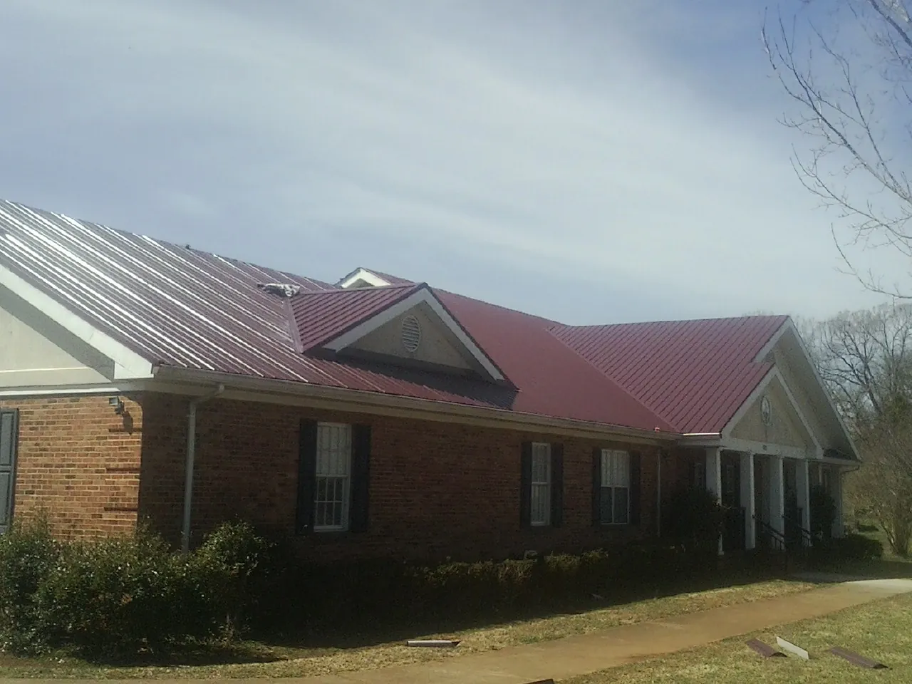 Red metal roof with gabled entries on a long brick building, from a Hail Damage Roof Repair job in Sopchoppy