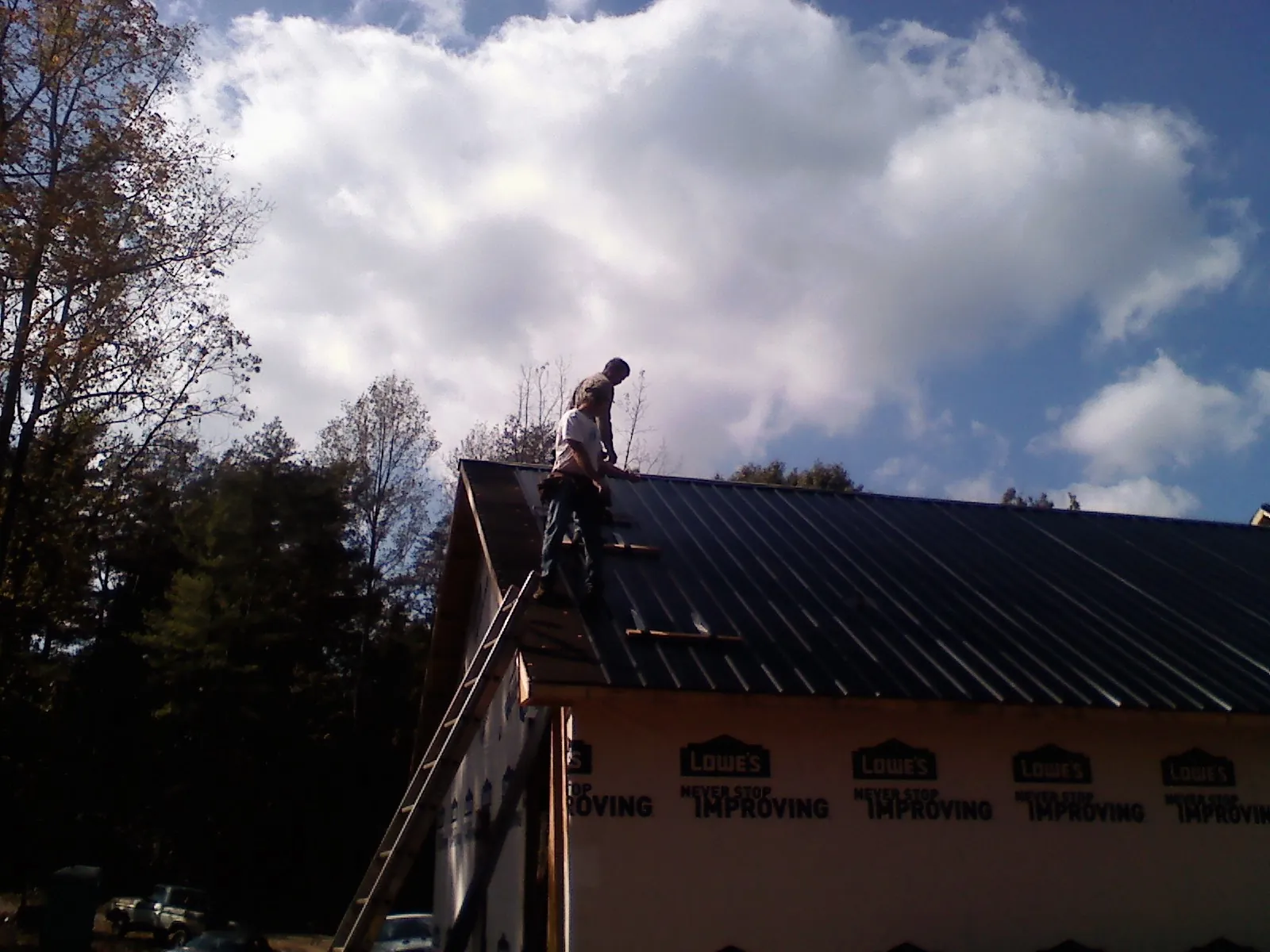 Roofer fastening dark metal panels high against a cloudy sky, from a Roof Inspection job in Sopchoppy