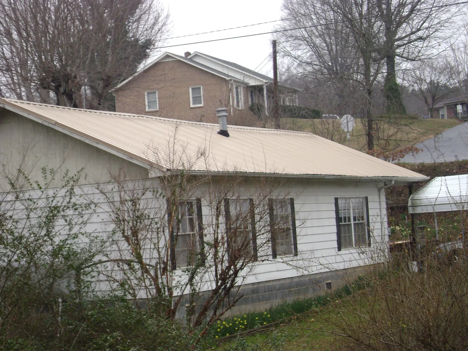 Tan metal roof on a white sided house set into a hillside — Commercial Roofing by Roofing Brothers in Sopchoppy